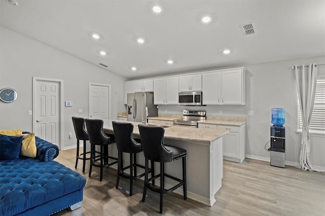 kitchen featuring white cabinets, appliances with stainless steel finishes, light hardwood / wood-style floors, a kitchen island with sink, and a breakfast bar