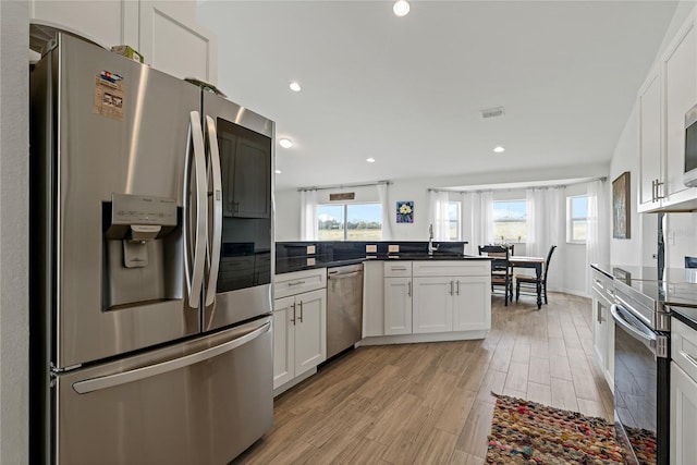 kitchen with kitchen peninsula, plenty of natural light, appliances with stainless steel finishes, white cabinetry, and sink