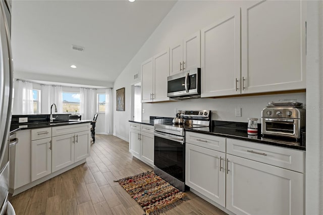 kitchen featuring sink, stainless steel appliances, vaulted ceiling, and white cabinetry