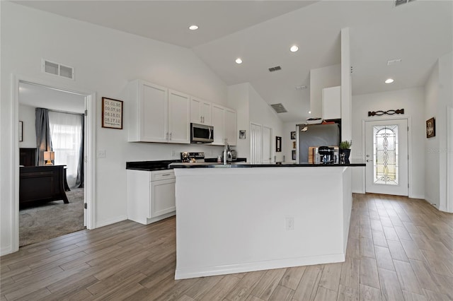 kitchen featuring appliances with stainless steel finishes, white cabinets, lofted ceiling, and a center island with sink