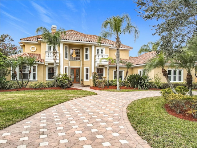 mediterranean / spanish home with a balcony, a front yard, and french doors