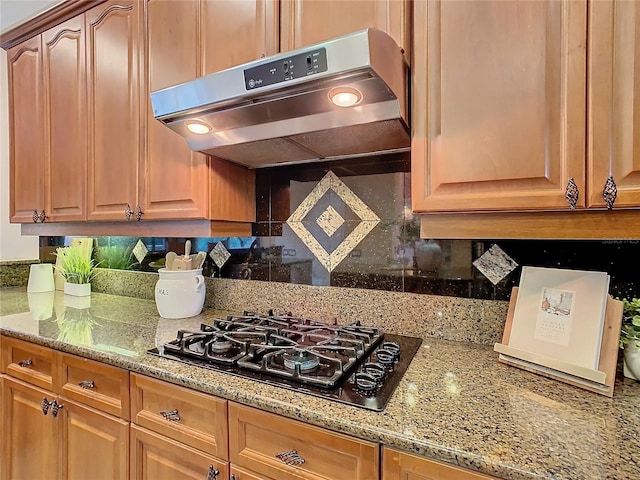 kitchen featuring range hood, decorative backsplash, light stone counters, and black gas stovetop