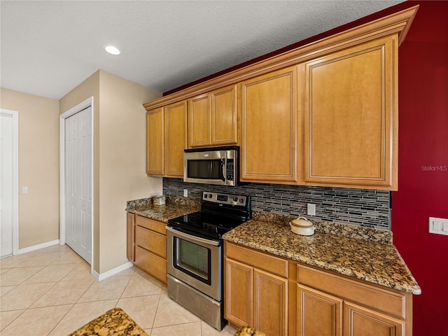 kitchen with light tile patterned floors, appliances with stainless steel finishes, dark stone counters, and tasteful backsplash