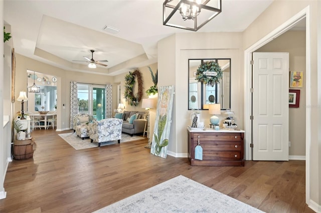 foyer featuring ceiling fan with notable chandelier, wood-type flooring, and a raised ceiling