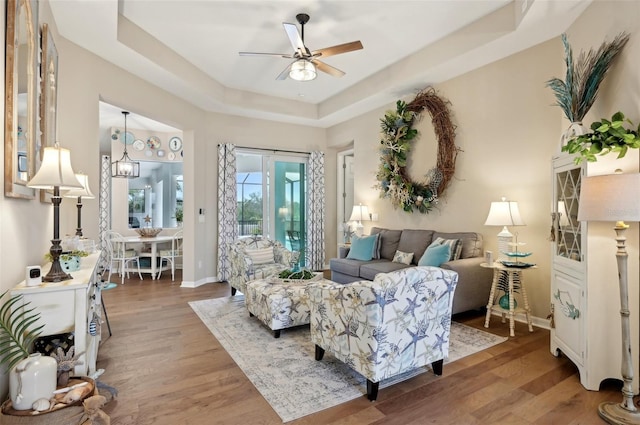 living room with hardwood / wood-style flooring, a raised ceiling, and ceiling fan