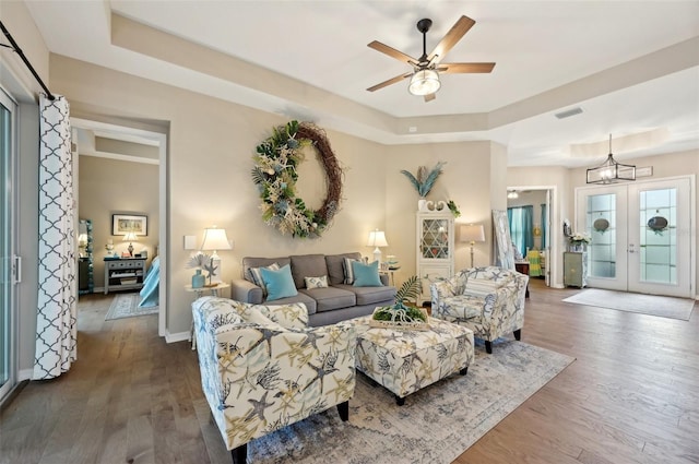 living room featuring french doors, hardwood / wood-style floors, ceiling fan with notable chandelier, and a raised ceiling