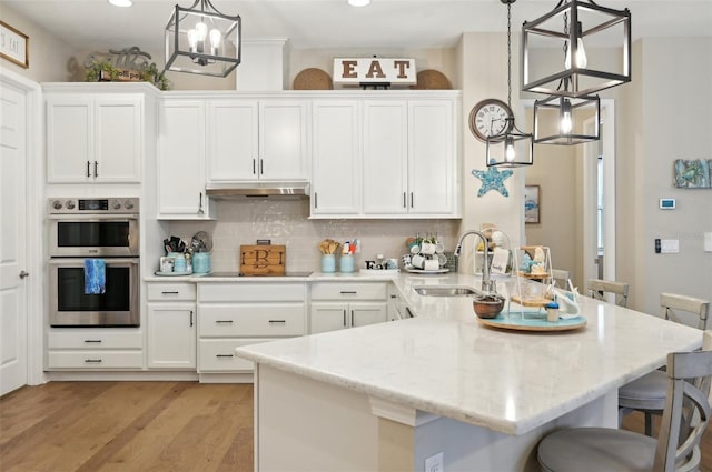 kitchen featuring pendant lighting, stainless steel double oven, decorative backsplash, sink, and a kitchen breakfast bar