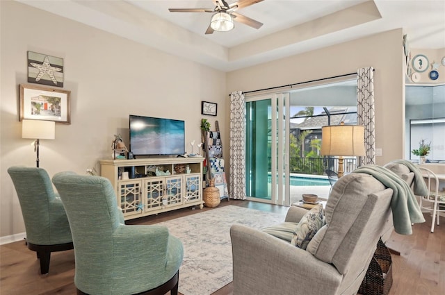 living room with ceiling fan, hardwood / wood-style flooring, and a tray ceiling