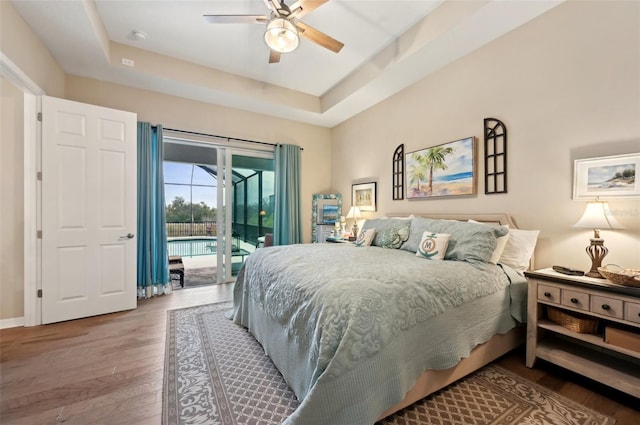 bedroom with ceiling fan, access to exterior, a tray ceiling, and hardwood / wood-style flooring