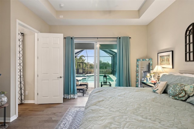 bedroom featuring wood-type flooring, a raised ceiling, and access to outside