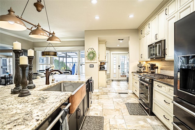 kitchen with plenty of natural light, tasteful backsplash, hanging light fixtures, light stone countertops, and black appliances