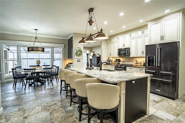 kitchen featuring a kitchen island with sink, premium appliances, white cabinets, and decorative light fixtures