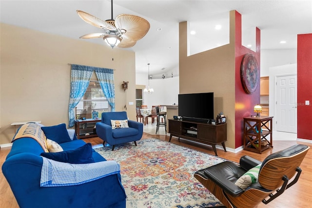 living room with ceiling fan with notable chandelier, wood-type flooring, and high vaulted ceiling