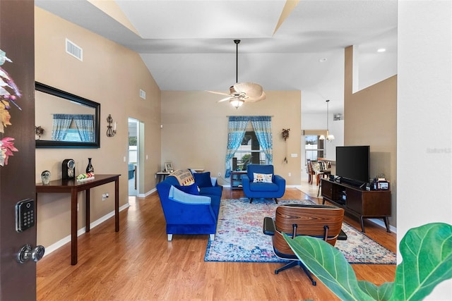 living room with ceiling fan with notable chandelier, wood-type flooring, and high vaulted ceiling