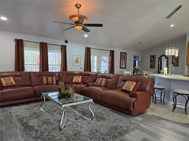 living room featuring ceiling fan, vaulted ceiling, light hardwood / wood-style floors, sink, and french doors