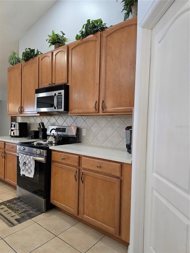 kitchen featuring light tile patterned flooring, lofted ceiling, stainless steel appliances, and tasteful backsplash