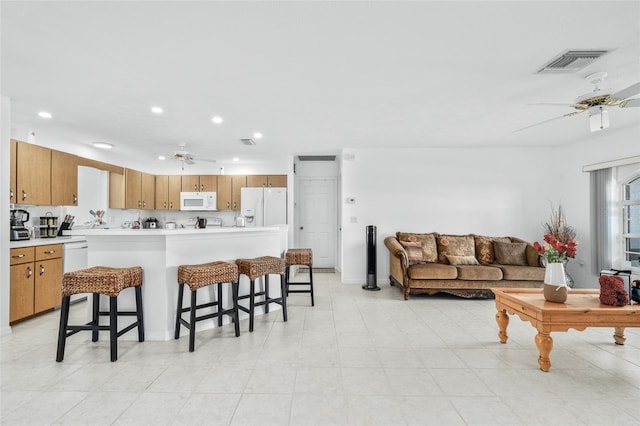 kitchen with a kitchen bar, white appliances, and ceiling fan