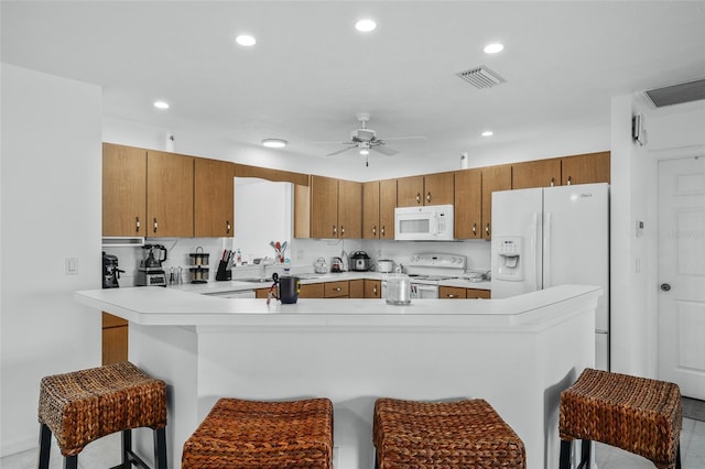 kitchen with ceiling fan, white appliances, kitchen peninsula, and a breakfast bar area