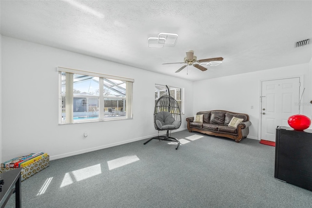 living area featuring ceiling fan, carpet, and a textured ceiling