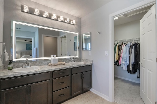 bathroom featuring a walk in closet, a sink, baseboards, and double vanity