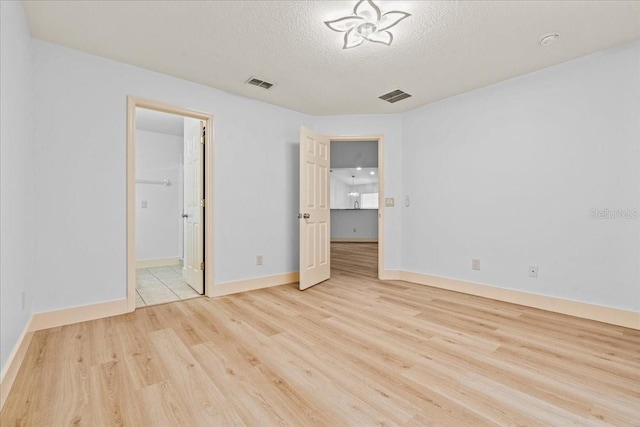 unfurnished bedroom with light hardwood / wood-style floors, a textured ceiling, and a walk in closet