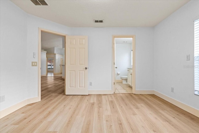 unfurnished bedroom featuring light wood-type flooring and ensuite bath