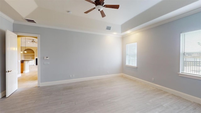 spare room featuring light wood-type flooring, ceiling fan, ornamental molding, and a raised ceiling