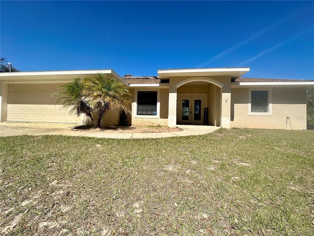 view of front of home featuring french doors, stucco siding, an attached garage, driveway, and a front lawn