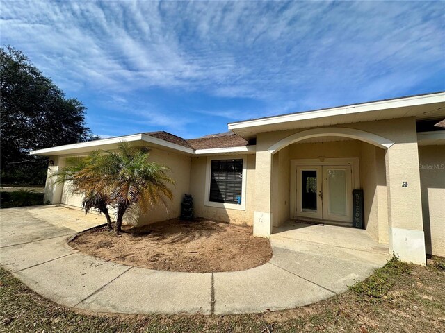 doorway to property with french doors, an attached garage, and stucco siding