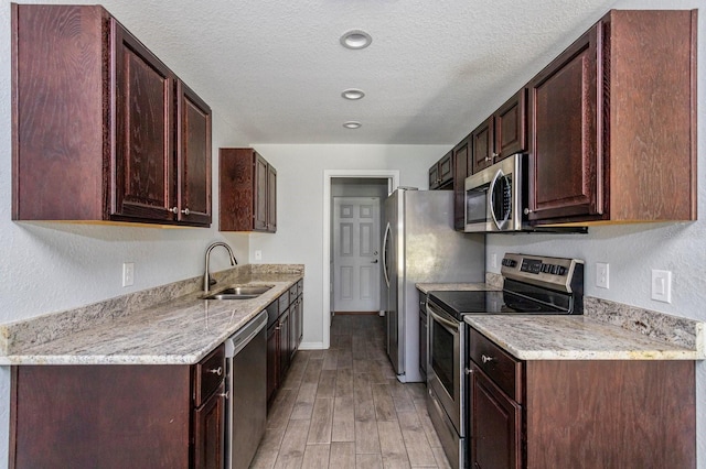 kitchen with appliances with stainless steel finishes, sink, a textured ceiling, and light hardwood / wood-style floors