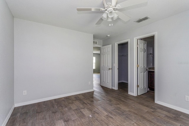 unfurnished bedroom featuring a walk in closet, dark hardwood / wood-style floors, ceiling fan, and a closet