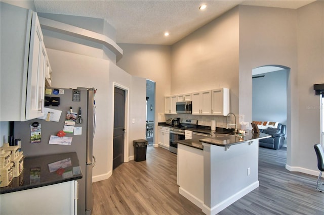 kitchen with appliances with stainless steel finishes, a breakfast bar, white cabinets, a high ceiling, and kitchen peninsula