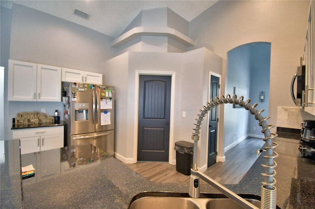 kitchen with appliances with stainless steel finishes, high vaulted ceiling, white cabinetry, dark stone countertops, and hardwood / wood-style flooring