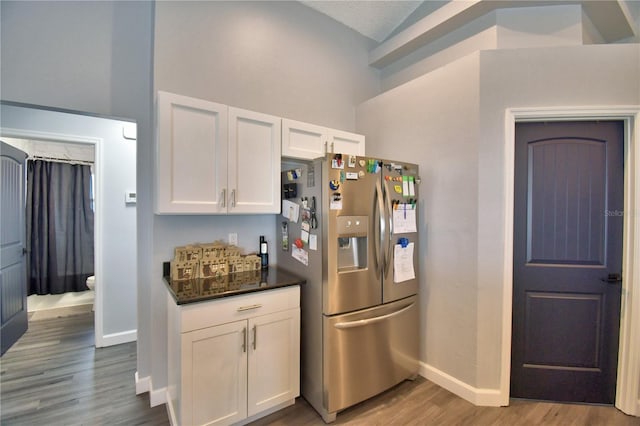 kitchen featuring stainless steel refrigerator with ice dispenser, white cabinetry, wood-type flooring, and vaulted ceiling