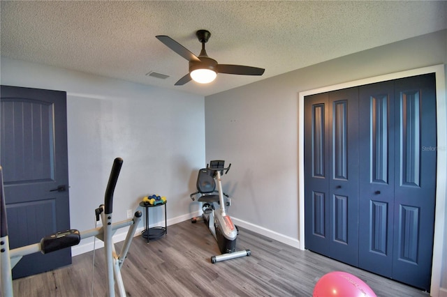 workout area with ceiling fan, wood-type flooring, and a textured ceiling