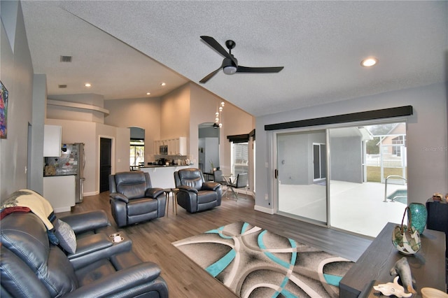 living room with wood-type flooring, high vaulted ceiling, ceiling fan, and a textured ceiling