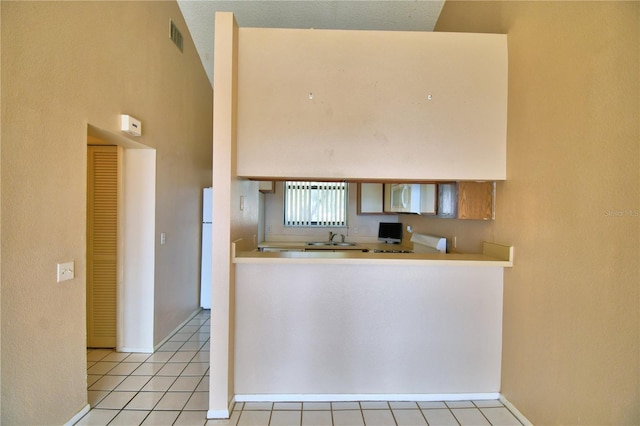 kitchen featuring light tile patterned flooring, a towering ceiling, white refrigerator, and sink