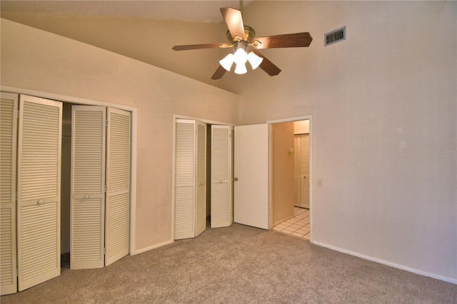 unfurnished bedroom featuring ceiling fan, lofted ceiling, light colored carpet, and two closets