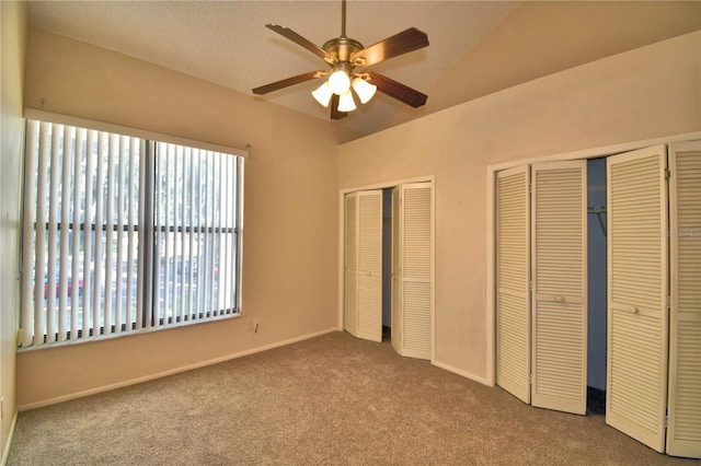 unfurnished bedroom featuring light colored carpet, vaulted ceiling, multiple closets, ceiling fan, and multiple windows