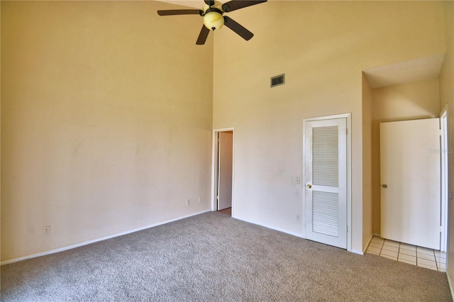 unfurnished bedroom with ceiling fan, light carpet, and a towering ceiling