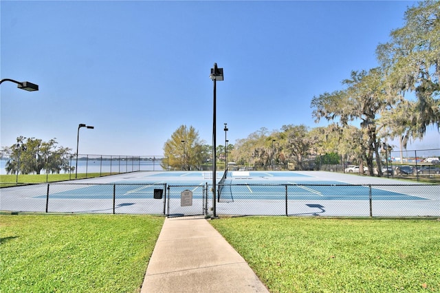 view of sport court with a water view and a lawn