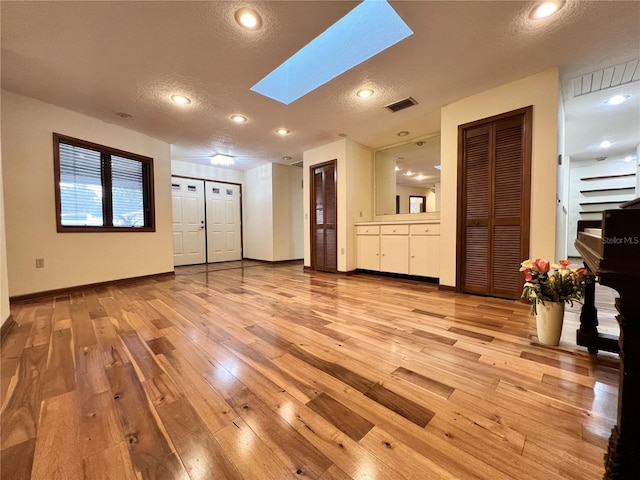 unfurnished living room featuring light wood-type flooring, a textured ceiling, and a skylight