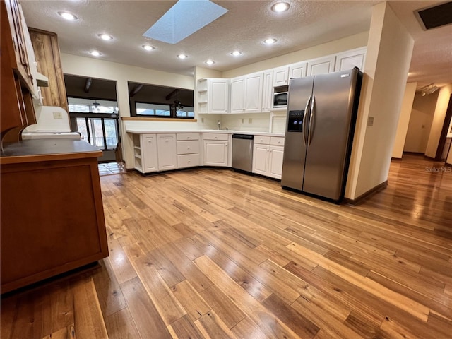 kitchen with white cabinetry, a skylight, light wood-type flooring, appliances with stainless steel finishes, and kitchen peninsula