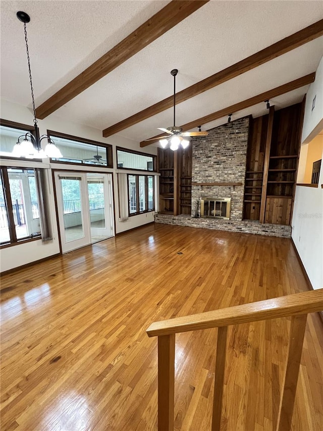 unfurnished living room with ceiling fan with notable chandelier, a fireplace, light hardwood / wood-style floors, a textured ceiling, and beam ceiling