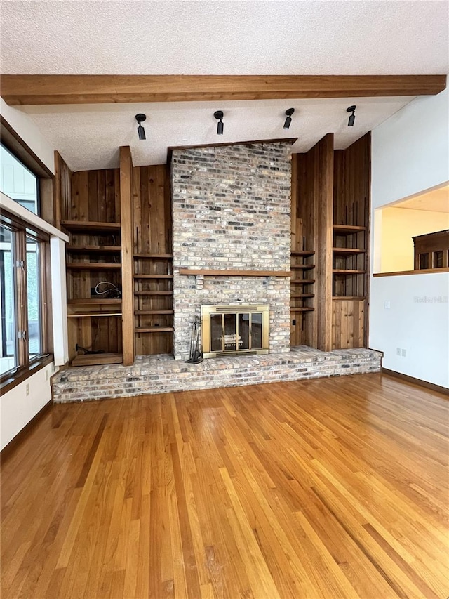 unfurnished living room featuring built in shelves, a fireplace, a textured ceiling, and wood walls