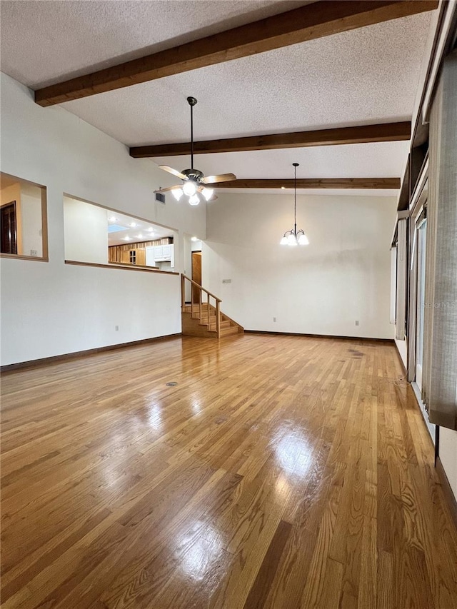 unfurnished living room featuring lofted ceiling with beams, ceiling fan with notable chandelier, a textured ceiling, and light hardwood / wood-style flooring