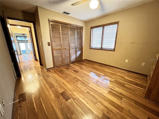 unfurnished bedroom with a textured ceiling, a closet, ceiling fan, and light wood-type flooring