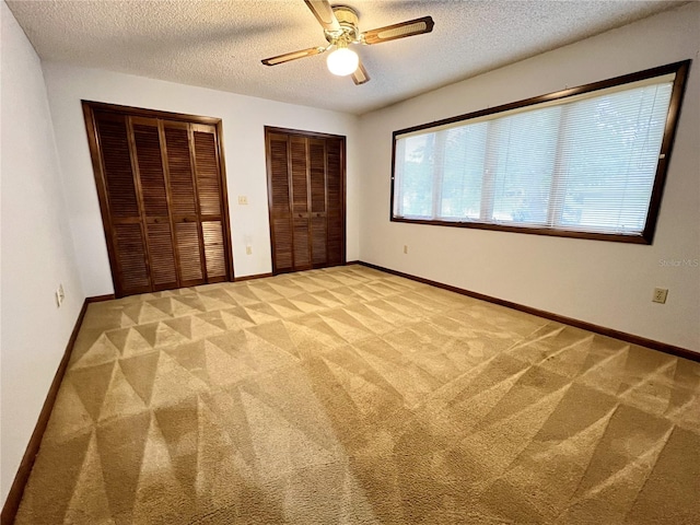 unfurnished bedroom featuring multiple closets, light colored carpet, a textured ceiling, and ceiling fan