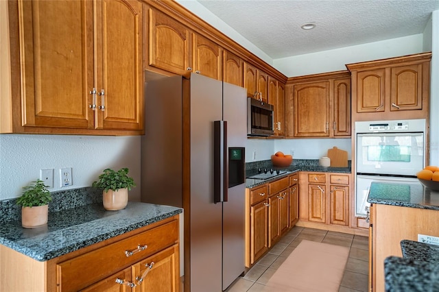 kitchen with light tile patterned floors, double oven, a textured ceiling, black electric cooktop, and stainless steel fridge with ice dispenser