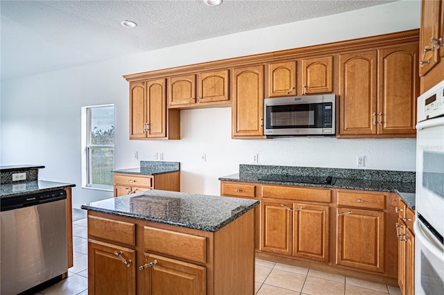 kitchen featuring light tile patterned floors, appliances with stainless steel finishes, dark stone countertops, a textured ceiling, and a kitchen island